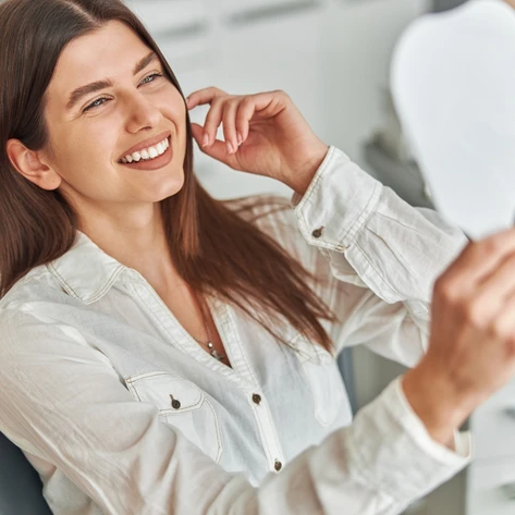Happy cosmetic dentistry patient looking at her smile in mirror