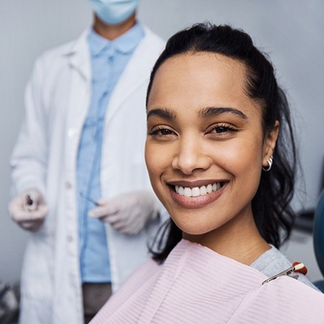 A smiling young woman and her dentist in the background