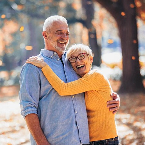 An older, smiling man and his smiling wife in an autumn setting