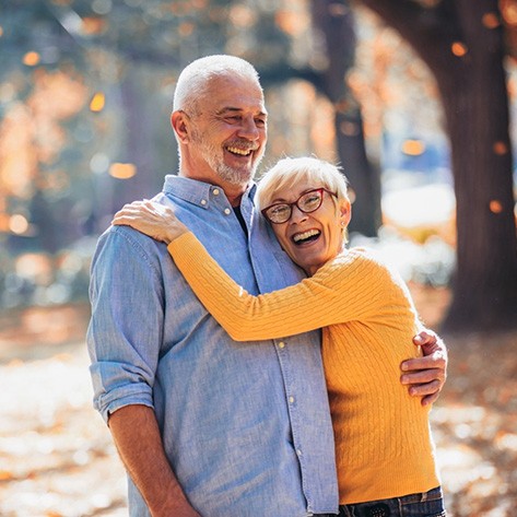 An older, smiling man and his smiling wife in an autumn setting while wearing dentures in Dracut
