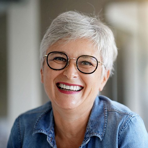 Older woman with black rimmed glasses showing off her dentures in Dracut