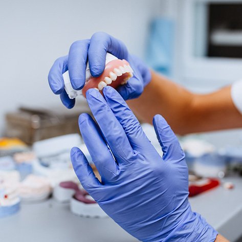 A closeup of upper dentures being held by gloved hands