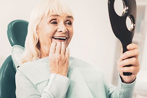 A smiling senior woman admiring her dentures with a hand mirror